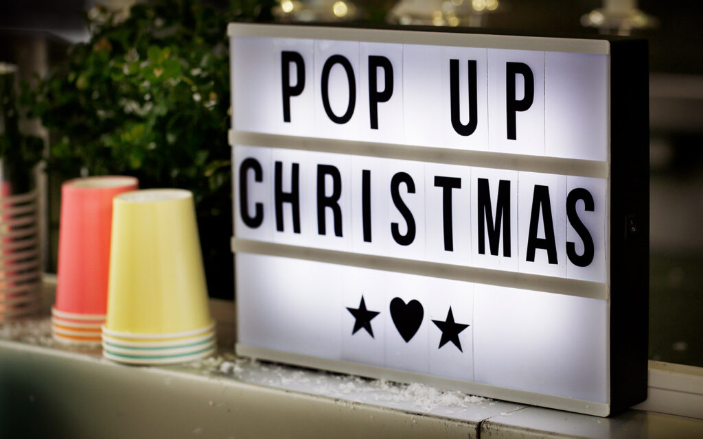 En ljusskylt med texten "Pop up Christmas". Bredvid står staplar med pappmuggar i olika färger.
