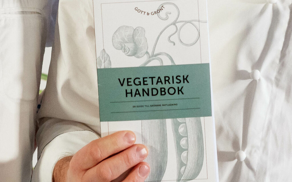 Närbild på en kock som håller upp en kopia av Vegetarisk Handbok - Gott och Grönt.